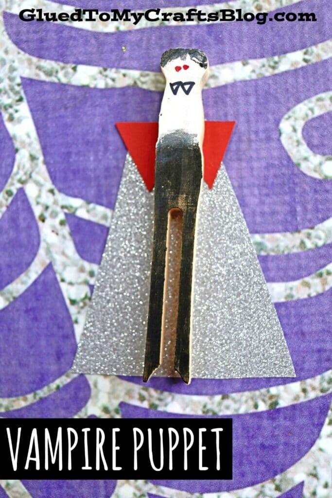 A halloween clothespin puppet decorated as a vampire, featuring a painted face, red bow tie, red paper collar, and a sparkly silver cape on a purple patterned background. The text VAMPIRE PUPPET is at the bottom.