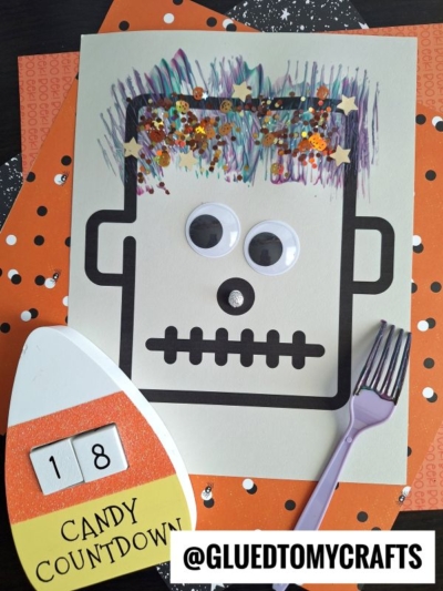 A Halloween craft features a Frankenstein face with fork painted monster hair, googly eyes, glitter, and stars. A candy countdown sign, orange papers with black dots, and a purple fork are also included.