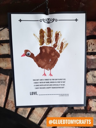 A handmade handprint turkey drawing using a brown handprint as the body, with googly eyes and a beak drawn on. Below, a sweet Thanksgiving message or handprint turkey poem is written, and the handle @GLUEDTOMYCRAFTS appears at the bottom right.