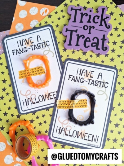Two Halloween cards say “Have a fang-tastic Halloween!” Each holds a playful vampire fang and festive washi tape. Decorated in orange, black, and green, with twinkling stars and a cheerful Trick or Treat sign, these cards are perfect for sharing some fang-tastic Halloween fun. @GLUEDTOMYCRAFTS text is at the bottom.