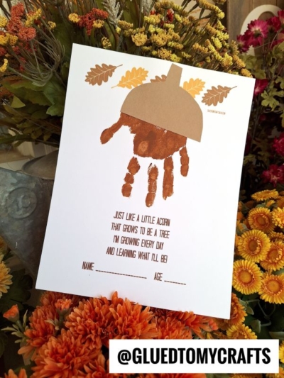 A fall-themed craft featuring a handprint acorn poem: a brown handprint shaped like an acorn, decorated with paper leaves. Below is a sweet poem about growing, with spots for your child's name and age, set against colorful autumn flowers.