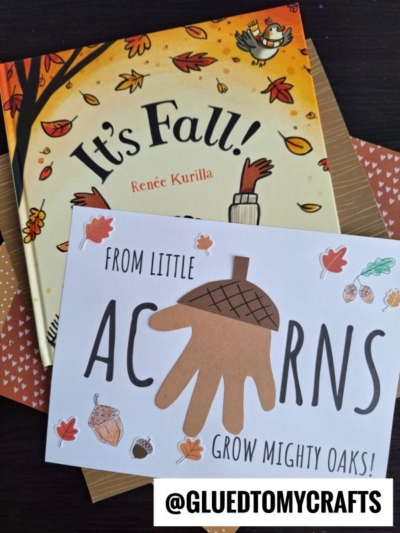 A fall-themed children's book titled Its Fall! sits beside a handmade card featuring a handprint acorn poem—From little acorns grow mighty oaks!—decorated with an acorn illustration and autumn leaves. @GLUEDTOMYCRAFTS is at the bottom.