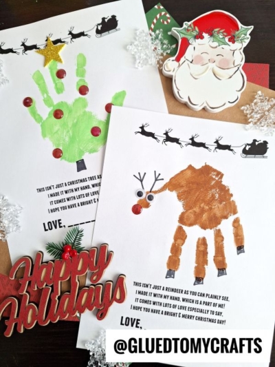 Two festive handprint crafts on paper: one green handprint decorated with a star and buttons, the other brown with reindeer features. Santa, Happy Holidays cutouts, and sweet handprint holiday poems complete the cheerful scene. @GLUEDTOMYCRAFTS is visible.