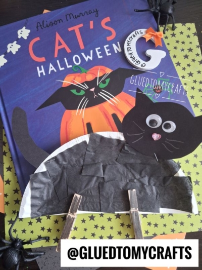 Children’s Halloween craft featuring a clothespin black cat made from paper and clothespins, with googly eyes, displayed on a Cats Halloween book cover. This adorable project is perfect for making your own paper plate cat or clothespin cat at home. Decorative spiders and a @GLUEDTOMYCRAFTS sticker are also present.