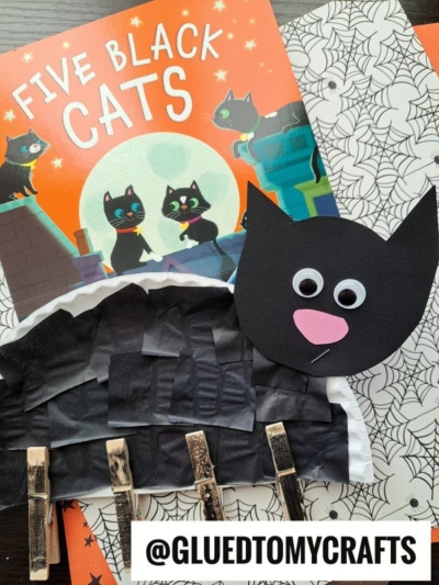 Childrens craft scene with the book Five Black Cats, a cat face made of paper with googly eyes, a clothespin black cat craft on spider web paper, and an adorable paper plate cat. The @GLUEDTOMYCRAFTS handle is visible at the bottom.