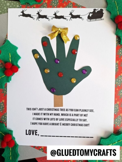 A Christmas craft featuring a green handprint cutout decorated as a tree with colorful glitter dots and a gold bow, placed on a card with handprint holiday poems and holly decorations around the border.