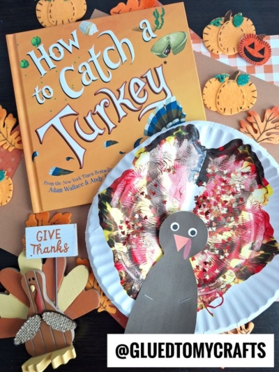 A children’s book titled How to Catch a Turkey sits on a table surrounded by paper pumpkins. In front are two colorful turkey crafts: one with a cupcake liner as feathers and another made with clothespins and felt. @GLUEDTOMYCRAFTS.