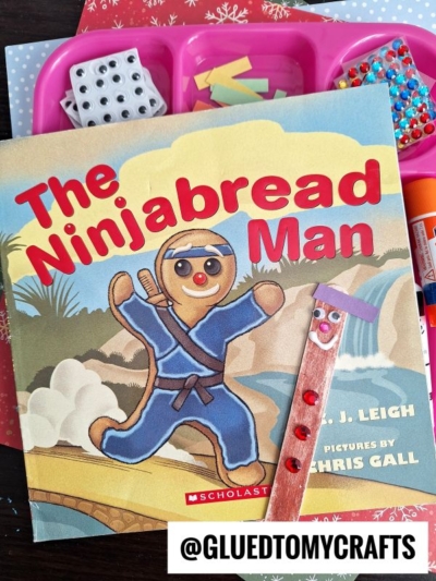 A children’s book titled The Ninjabread Man is surrounded by craft supplies, including popsicle stick ninjabread men, colored beads, small blocks, and glue. The Instagram handle @GluedToMyCrafts is visible.