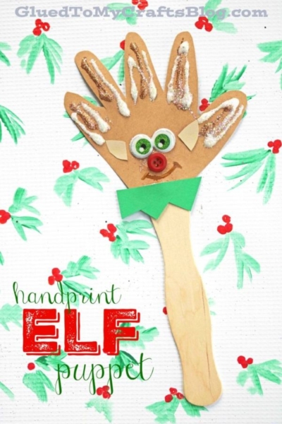 A handprint elf puppet made from brown paper, googly eyes, red pom-pom nose, red button mouth, and green collar on a wooden stick. Christmas holly patterns decorate the white background—a festive addition to any Handprint Christmas Puppets collection.