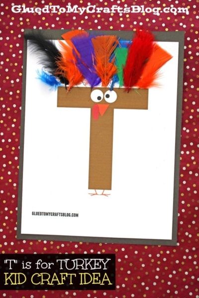 A paper turkey craft features the letter T made from brown paper, decorated with colorful feathers, googly eyes, and an orange beak to resemble a turkey. The red background with gold dots adds a festive touch. Perfect for "T is for Turkey" activities!.