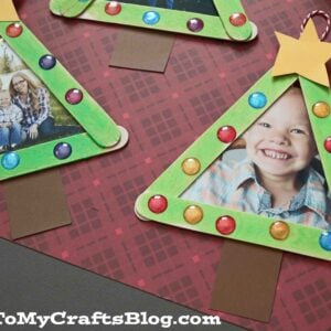 Two handmade popsicle stick Christmas tree frame ornaments, painted green and decorated with colorful dots, stars on top, and brown trunks, each beautifully framing a cherished family photo.