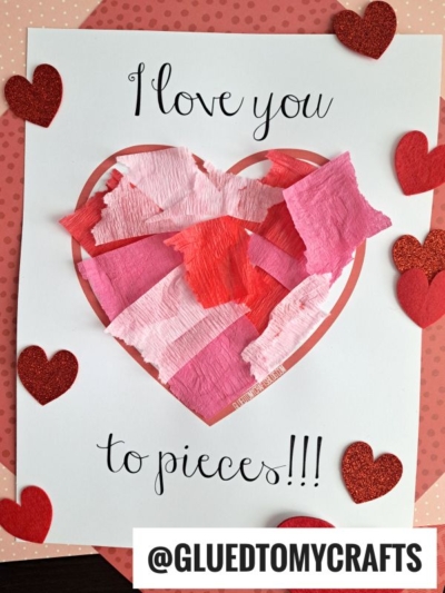 A Valentine’s i love you to pieces craft featuring a heart shape filled with paper scrap love you to pieces on white paper. The text reads I love you to pieces!!! and glittery red hearts decorate the background.