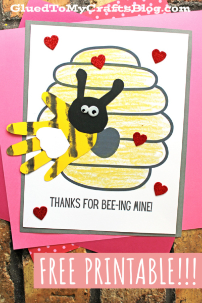 A handmade card features a yellow beehive, a handprint bee, and red glitter hearts. Text says “THANKS FOR BEE-ING MINE!” and “FREE PRINTABLE!” with a pink border—perfect as a sweet bee mine keepsake.