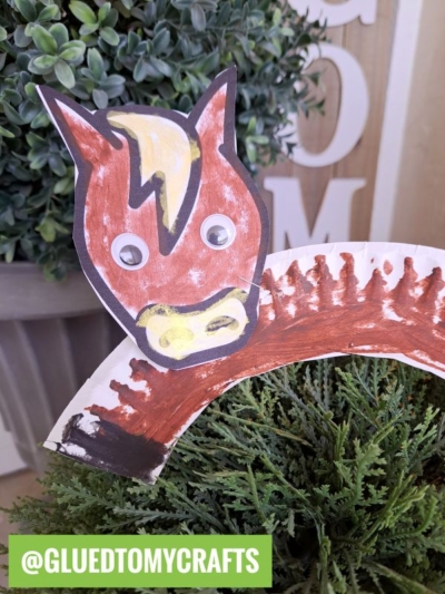 A paper plate horse craft, featuring a painted brown plate with a paper horse face and googly eyes, is set among green plants. The text @GLUEDTOMYCRAFTS appears at the bottom.