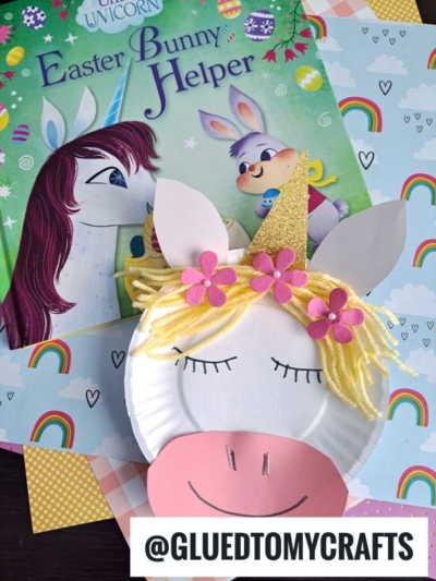 A unicorn-themed children’s book paired with a magical paper plate unicorn craft, made from yarn, felt, and glittery paper. The pastel paper background features rainbows and hearts. Text: @GLUEDTOMYCRAFTS.