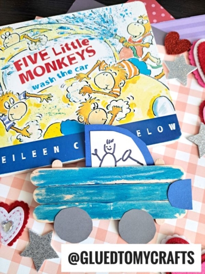 A handmade blue popsicle stick truck with paper wheels sits in front of the book Five Little Monkeys Wash the Car. Decorative felt hearts and silver stars are scattered around. @GLUEDTOMYCRAFTS tag is visible.