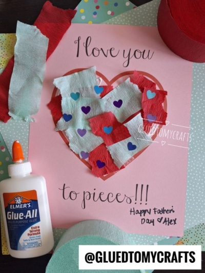 A handmade Fathers Day card featuring a heart shape filled with paper scrap love you to pieces, torn red and blue tissue, heart stickers, Elmers glue, and "I love you to pieces!!!" written on pink paper.