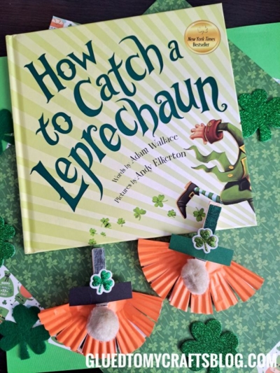 A book titled “How to Catch a Leprechaun” sits on a green surface, surrounded by glittery shamrocks and two adorable clothespin leprechaun crafts made from cupcake liners. The website “gluedtomycraftsblog.com” is at the bottom.