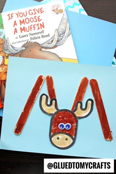 A craft project inspired by If You Give a Moose a Muffin. Create a popsicle stick moose face and antlers on blue paper, with the book and blue construction paper in the background for added charm.