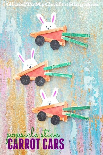 Three bunny crafts made from popsicle sticks, felt, and clothespins form adorable popsicle stick carrot cars with green clothespin stems and black wheels, displayed on a textured background.