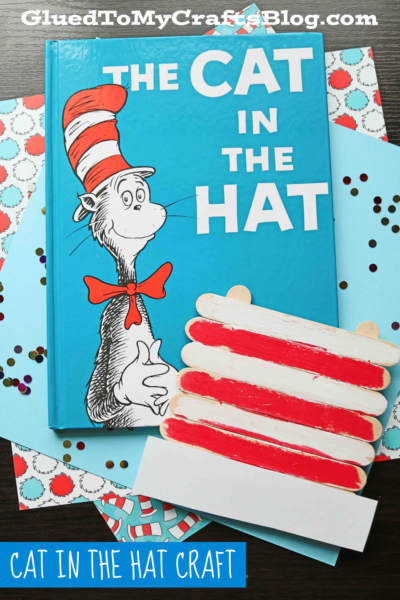 A blue book titled The Cat in the Hat sits on a decorated surface, next to a popsicle stick Seuss hat craft painted with red and white stripes, resembling the iconic hat from the story.
