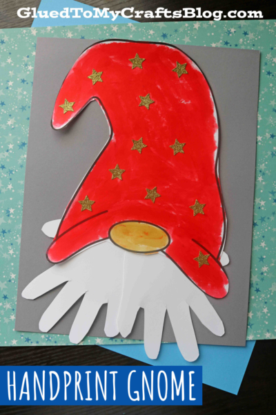 A child’s craft of a paper handprint gnome features a red hat decorated with gold stars and a beige oval nose, with a playful handprint beard made from white paper, all set on a gray and blue background. Text reads HANDPRINT GNOME.
