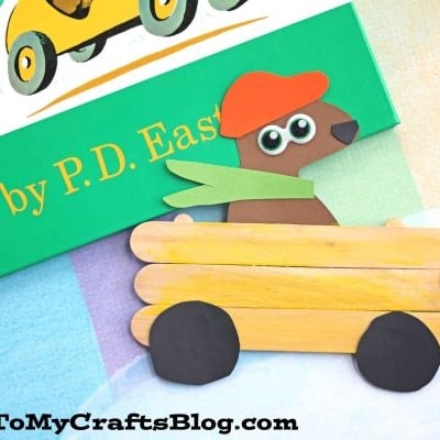 A children’s book titled “Go, Dog. Go!” by P.D. Eastman sits on a colorful background. Below it is a go dog go craft: a popsicle stick car with black wheels and a brown paper dog driver.