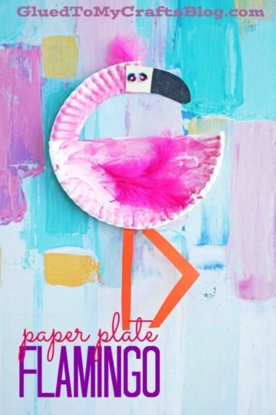 A vibrant paper plate flamingo craft, featuring fluffy pink feathers and cheerful orange paper legs, is displayed against a colorful painted background. The playful text reads "paper plate FLAMINGO," making this charming paper flamingo project perfect for kids' art activities.