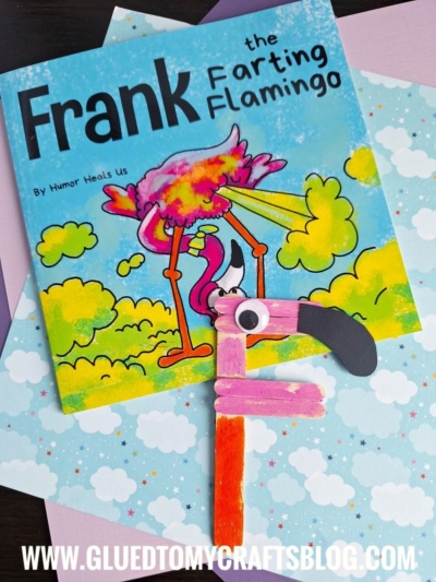 A children’s book titled Frank the Farting Flamingo is on a pastel cloud-themed background. Below the book, a flamingo craft for kids made from colored popsicle sticks is positioned to resemble the letter F, highlighting that “f is for flamingo.”.