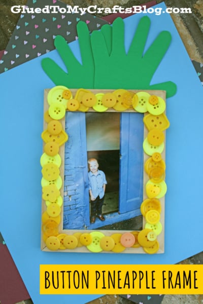 A handmade button pineapple frame, decorated with yellow buttons and topped with green paper leaves. A child’s photo stands inside, with the text “Button Pineapple Frame.” Craft blog branding appears above.