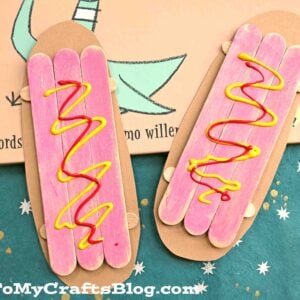 A children’s book titled The Pigeon Finds a Hot Dog! is shown with two popsicle stick hot dog crafts, each painted with pink centers and squiggles of yellow and red like mustard and ketchup.