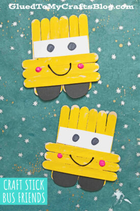 Two craft stick school bus crafts made from yellow-painted sticks, white paper windows, black paper wheels, googly eyes, and smiling faces on a teal background with small star patterns.