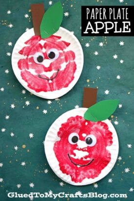 Two paper plates painted red with a playful paint splat apples effect, each with large googly eyes, a brown paper stem, and a green leaf, on a green star-patterned background. Text reads: Paper Plate Apple GluedToMyCraftsBlog.com.