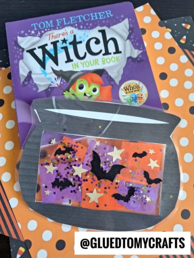 A children’s book titled There’s a Witch in Your Book sits behind a stained glass witch cauldron craft with orange and purple squares, black bat stickers, gold stars, and glitter on a polka dot background. Text: @GLUEDTOMYCRAFTS.