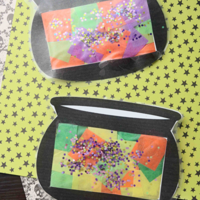 Two paper craft cauldrons with colorful tissue paper and glitter inside are displayed on patterned scrapbook paper. The text “Stained Glass Witch Cauldron” appears at the bottom.