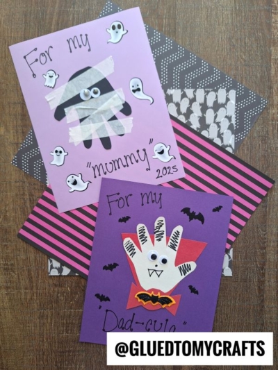 Two handmade Halloween cards for parents: one with a mummy design on pink paper, and one with a white handprint vampire on purple paper. Both cards include bats or ghosts, with For my mommy and For my Dad-cula written on them—perfect as heartfelt Halloween keepsakes to cherish year after year.