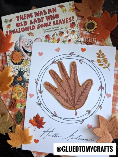 A children’s book, There Was an Old Lady Who Swallowed Some Leaves!, is shown with a fall-themed craft featuring a handprint leaf-shaped cutout, colorful felt leaves, and Hello Autumn text. The @GLUEDTOMYCRAFTS tag is at the bottom.
