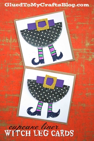 Two handmade Halloween cards featuring cupcake liner witch hats and skirts with polka dots, purple belts with gold buckles, and striped witch legs with black shoes, all on a vibrant red-orange background.