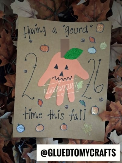 A handmade Halloween keepsake card on a bed of fall leaves with the text Having a gourd time this fall! and a handprint cutout decorated as a jack-o-lantern.