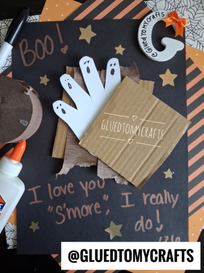A Halloween craft featuring ghost cutouts, a cardboard square with GLUEDTOMYCRAFTS, star stickers, glue, and “Boo! I love you s’more, I really do!” handwritten on black paper—perfect for creating adorable halloween keepsakes you’ll cherish year after year.