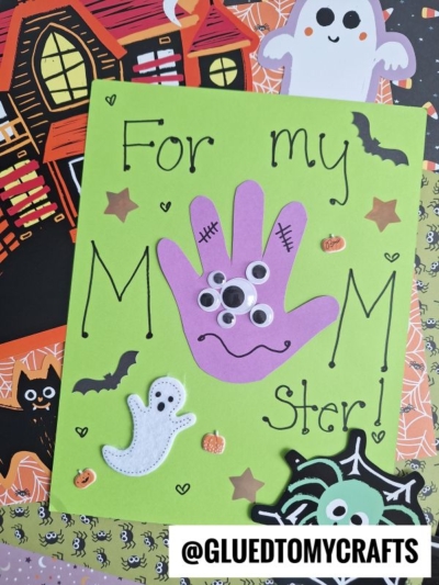A green card reads For my MUMMY ster! with a purple handprint decorated as a monster with googly eyes, surrounded by Halloween stickers and a spooky themed background—perfect for fun halloween keepsakes. @GLUEDTOMYCRAFTS.