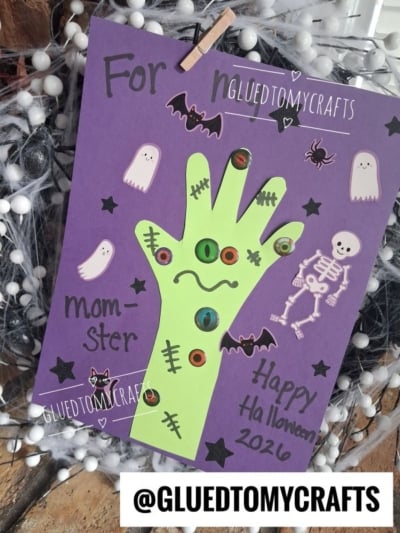 A purple Halloween craft features a green hand cutout with googly eyes, surrounded by ghost and skeleton stickers, with Happy Halloween 2016 written on it—making it a perfect addition to your collection of Halloween keepsakes.