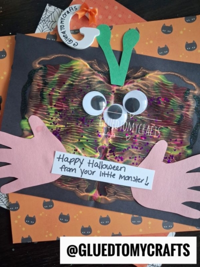 A colorful monster craft with googly eyes, handprint cutouts, and a Happy Halloween from your little monster! message on a Halloween-themed background—perfect for creating memorable halloween keepsakes. @GLUEDTOMYCRAFTS is written at the bottom.