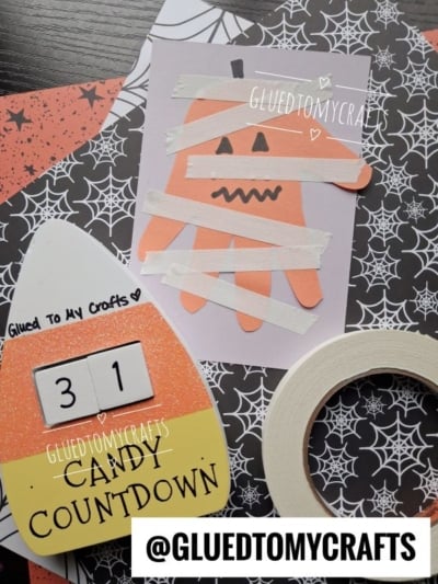 Halloween-themed crafts: a mummy made from an orange handprint with white tape, fun halloween keepsakes like a candy corn countdown calendar showing 31, decorative papers with webs and stars, and a roll of tape. @GLUEDTOMYCRAFTS at bottom.