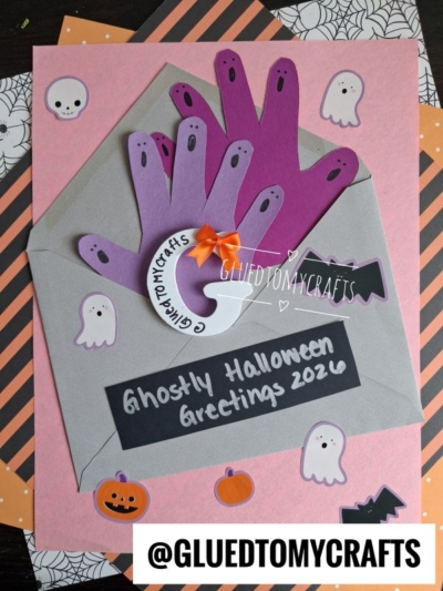 A Halloween card with purple handprint ghosts in a gray envelope, surrounded by ghost, pumpkin, and bat stickers, and the text “Ghostly Halloween Greetings 2020” — a delightful addition to your halloween keepsakes.