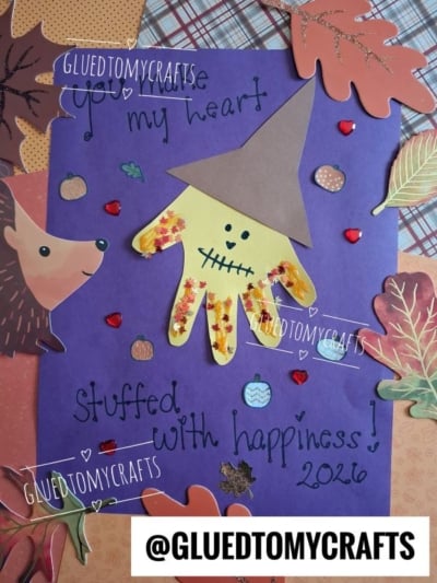 A purple card decorated with leaves, a hedgehog, and a yellow handprint scarecrow wearing a hat makes for charming Halloween keepsakes. The text reads, You make my heart stuffed with happiness! 2026. @GLUEDTOMYCRAFTS is at the bottom.
