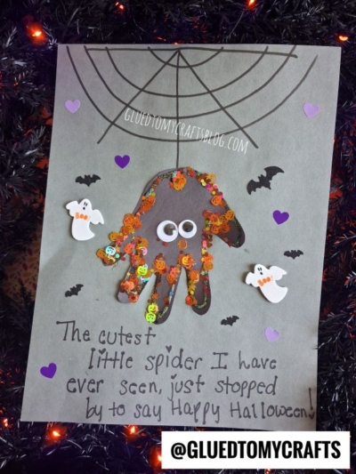 A Halloween craft shows a spider made from a handprint and orange sequins, with googly eyes. There are paper ghosts, bats, purple hearts, and a spider web—perfect halloween keepsakes for little hands. Text reads: The cutest little spider I have ever seen...