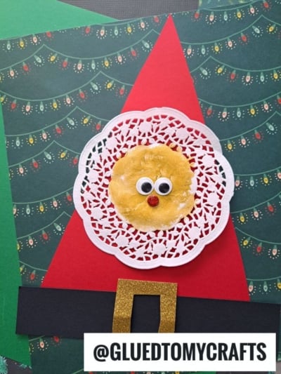A Christmas craft features a paper doily Santa suit background with a white doily and yellow circle as a face, googly eyes, and red nose. A gold belt buckle and @GLUEDTOMYCRAFTS text are at the bottom.