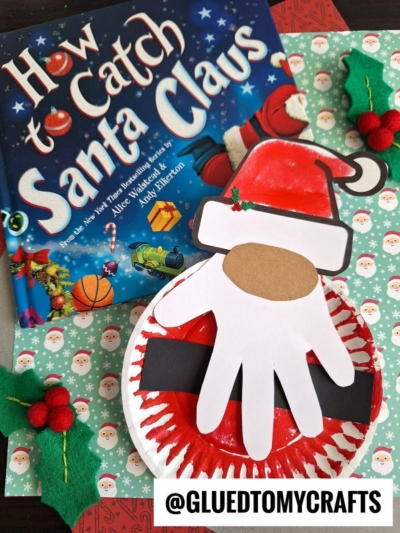A copy of the book How to Catch Santa Claus is next to a Santa craft, inspired by paper plate Christmas gnomes, featuring a red plate, a handprint beard, and Santa hat, all set on festive wrapping paper.