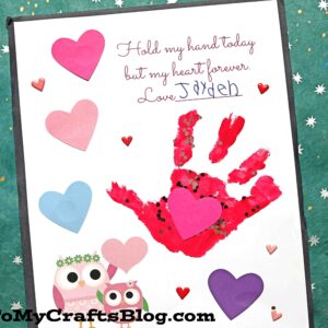A handmade Valentine’s card featuring “hold my hand today” with a red painted handprint, colorful paper hearts, two decorated owl cutouts, and the sweet message: “Hold my hand today but my heart forever. Love, Jayden.”